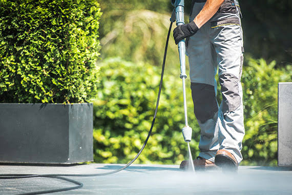 Power washing a paved outdoor surface beside landscaping
